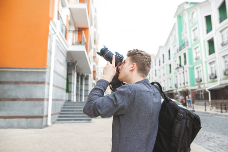 年轻人走在一个古老美丽的小镇的街道上, 手里拿着照相机, 照片建筑。时尚的旅游与背包的背部, 使照片架构