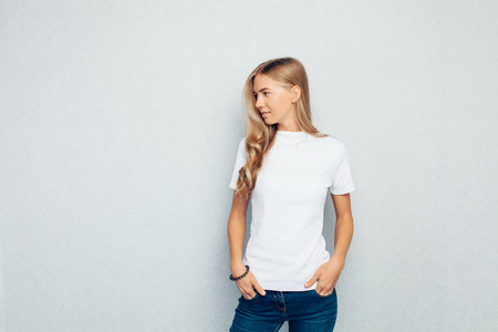 一个年轻漂亮的女孩身着白色 t恤站在灰色的墙壁背景姿势的形象