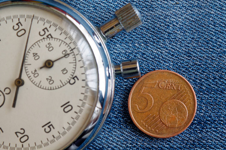 欧元硬币与面值5欧元美分和秒表在破旧的蓝色牛仔布背景商业背景