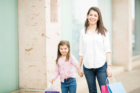 母亲和女儿站在商店背景五颜六色的购物袋