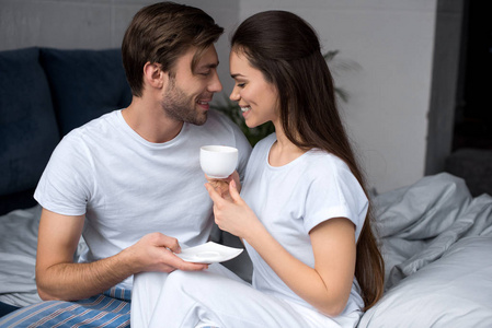 愉快的夫妇与咖啡拥抱在床上