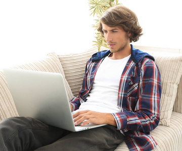 年轻人坐在沙发上的笔记本电脑上工作