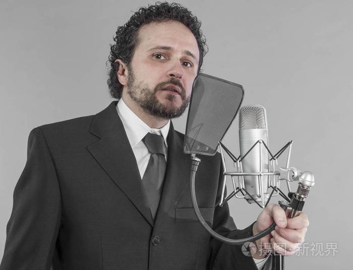 年轻男子的肖像与演播室麦克风唱歌.在灰色背景下隔离.歌手概念