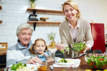 快乐的女人在她的丈夫和孙女的盘子里放新鲜的沙拉