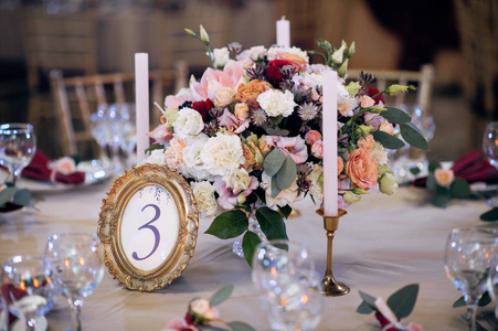 装饰桌子的黄金和勃艮第颜色与板材, 刀叉, 蜡烛和眼镜, 花束与花卉和绿色的中心