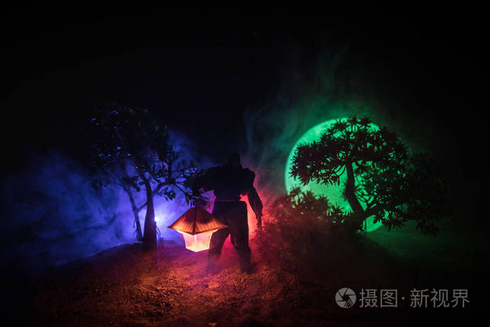 雨衣的男子从黑暗的森林里带着发光的灯笼在他的手概念一个恐怖杀手的