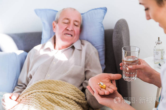 老病人躺在床上, 医生坐在他身旁, 给他吃药和水。