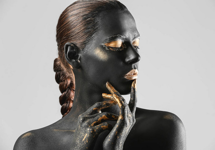 美丽的妇女与黑色和金色的油漆在她的身体与光背景