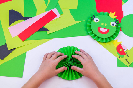 那孩子用纸做青蛙。青蛙公主是绿色的冠。儿童大师班。学校和幼儿园