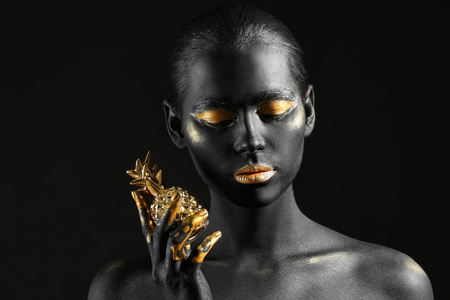 美丽的妇女与黑色和金色的油漆在她的身体与黑暗背景