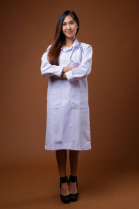 年轻美丽的亚洲妇女医生反对棕色背景