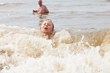 年轻的男孩和爷爷在海洋中游泳。享受海浪