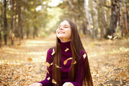迷人的女孩玩秋叶。青少年在秋季公园阳光明媚的一天的肖像