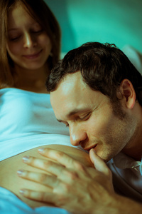 图像的幸福未来爸爸亲吻他怀孕的妻子的肚子