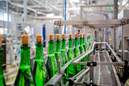 葡萄酒瓶与香槟在葡萄和起泡酒工厂的传送带上移动照片