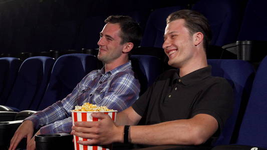 两个男朋友在电影院看喜剧片时大笑。