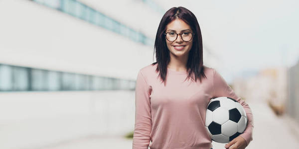 年轻漂亮的女人笑着开心, 拿着足球, 竞争的态度, 兴奋地在大学校园里玩游戏。
