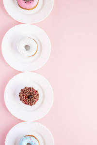 粉红色桌子上白色盘子上覆盖着釉面的甜甜圈