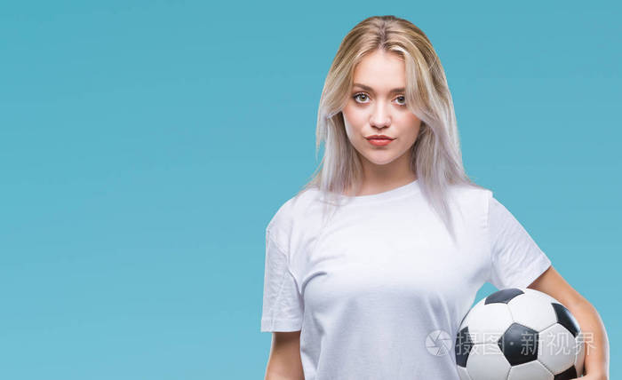 年轻的金发女子持有足球足球球在孤立的背景与自信的表情在聪明的脸思考严重