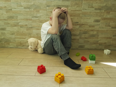 小可怜的男孩坐在地板上用一块块, 泰迪熊玩具照片