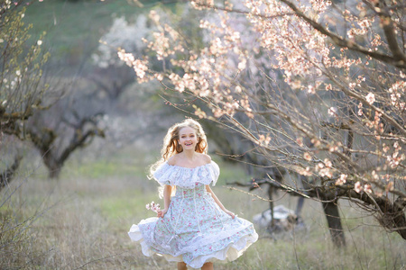 美丽的金发女孩穿着蓝色的礼服摆在盛开的花园