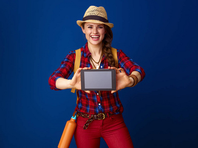 快乐活泼的妇女徒步旅行者在格子衬衣显示平板电脑空白屏幕在蓝色被隔绝了