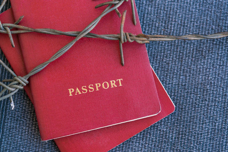 红色护照背后的铁丝网在蓝色的纺织品背景, 特写