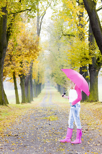 女人穿橡胶靴与伞在秋季巷子里