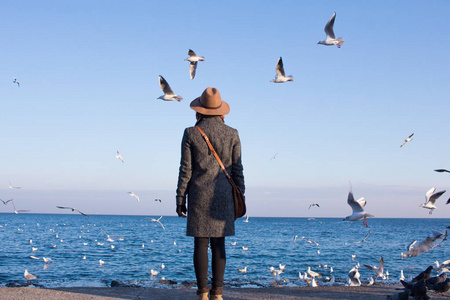秋天海滩上的年轻女子站在阳光明媚的日子, 看海鸥