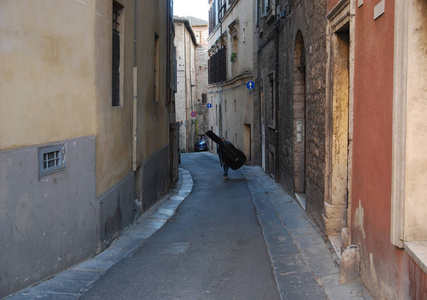 一个带着双低音的男人, 沿着佩鲁贾狭窄的街道走着。翁布里亚, 意大利