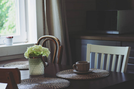 舒适的夏日早晨在乡间别墅的厨房。木桌上放着鲜花的花束, 开着架子。室内灰色和褐色的休闲早餐