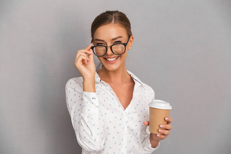 美丽的商业女性形象站在灰色墙边喝咖啡戴眼镜