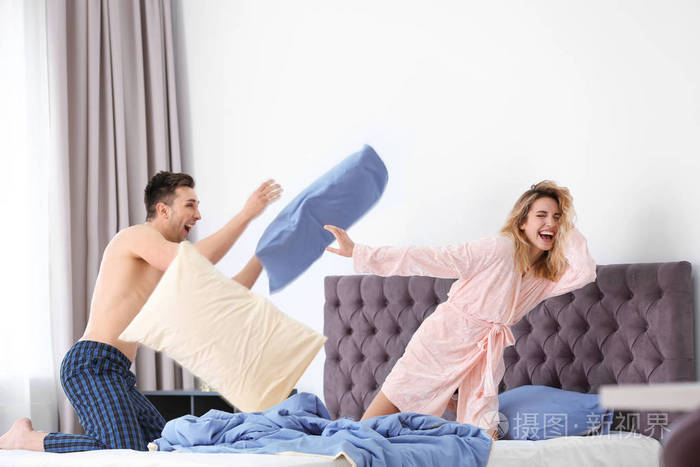 可爱的年轻夫妇在床上枕头打架在家