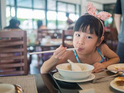 愉快的亚洲孩子吃美味的面条用筷子, 在
