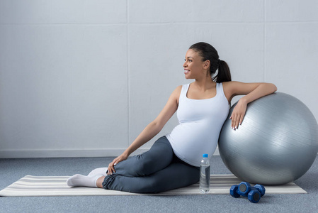 非洲裔美国人怀孕妇女坐在与水和哑铃适合球照片