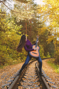 美丽的女孩与声学吉他在秋季公园。在铁路的青少年吉他