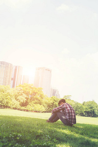 年轻的时髦男子坐在草地上独自对公园