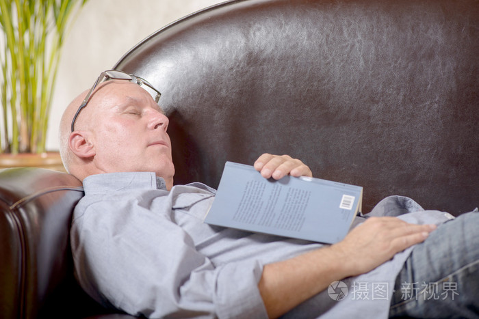 一位高级拿着一本书坐在沙发上睡着了