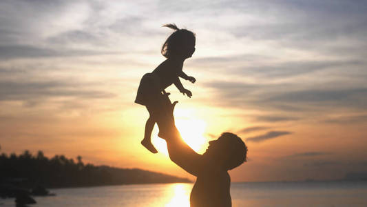 愉快的父亲和女儿的剪影在热带海滩一起演奏在惊人的日落照片