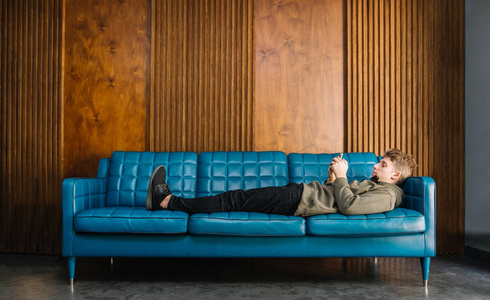 年轻人躺在沙发上, 看着木质背景的电话.