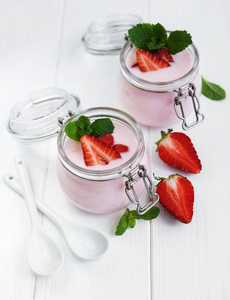 白色木桌上的草莓酸奶罐