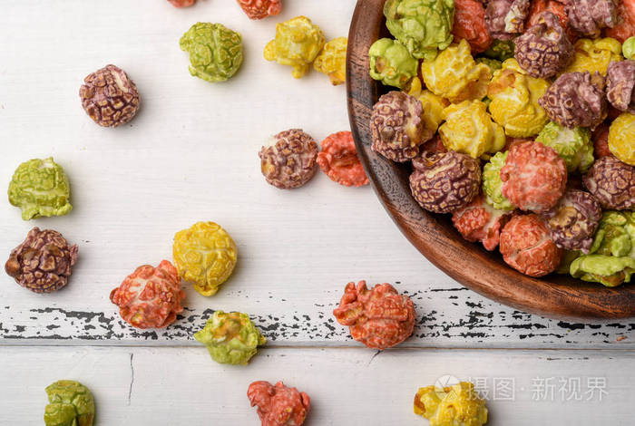 彩色焦糖爆米花在一个木碗上的白色木背