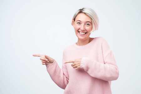 微笑的年轻女子指着手指离开孤立在灰色背景