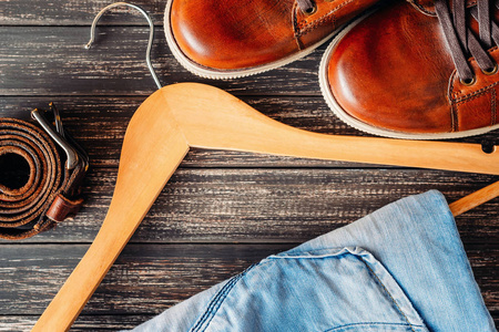 棕色皮革休闲鞋, 牛仔裤上 hangerand 带上木质背景的顶部景色。时尚理念