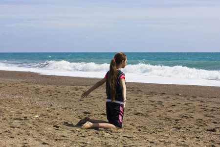 年轻的女孩坐在海滩附近的蓝色海