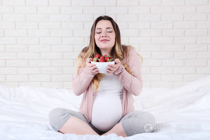 美丽的孕妇与草莓在碗里坐在床上