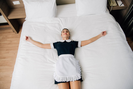 高视角的年轻美丽的女仆穿着制服躺在床上的酒店套房