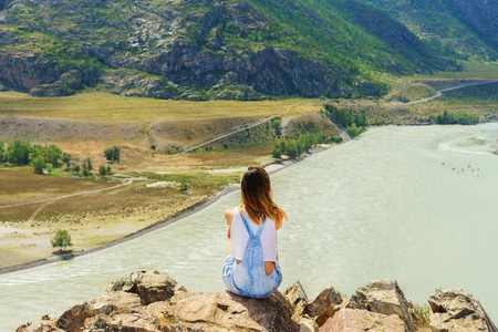 一个女孩坐在山上的岩石上。山顶上的游客。山河。夏日