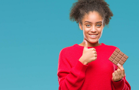 年轻的美国黑人妇女吃巧克力酒吧在孤立的背景下高兴与大微笑做 ok