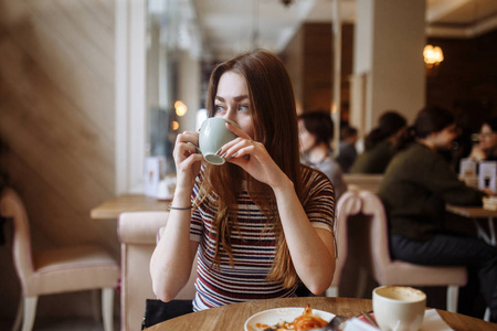 喝咖啡的美丽的年轻妇女坐在桌在咖啡馆